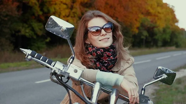 Jovem com cabelo castanho senta-se em uma moto perto de uma estrada . — Fotografia de Stock