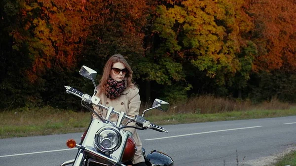 Junges Mädchen mit braunen Haaren sitzt auf einem Motorrad in der Nähe einer Straße. — Stockfoto