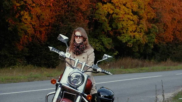 Chica joven con el pelo castaño se sienta en una moto cerca de una carretera . — Foto de Stock