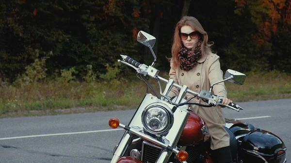 Chica joven con el pelo castaño se sienta en una moto cerca de una carretera . — Foto de Stock