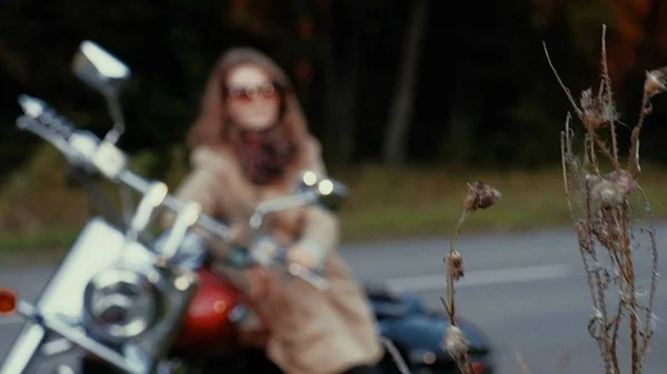 Ung tjej med brunt hår sitter på en motorcykel nära en väg. — Stockfoto