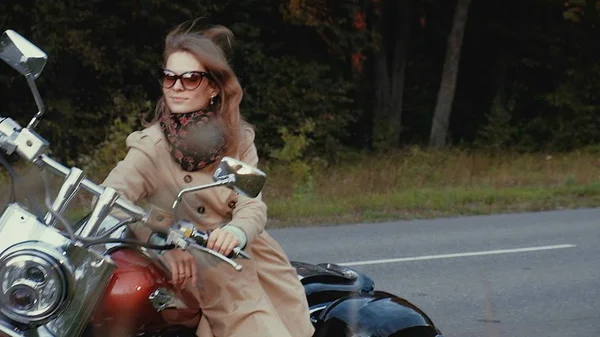 Молодая девушка с каштановыми волосами сидит на мотоцикле возле дороги . — стоковое фото