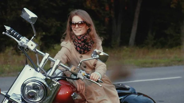 Jovem com cabelo castanho senta-se em uma moto perto de uma estrada . — Fotografia de Stock
