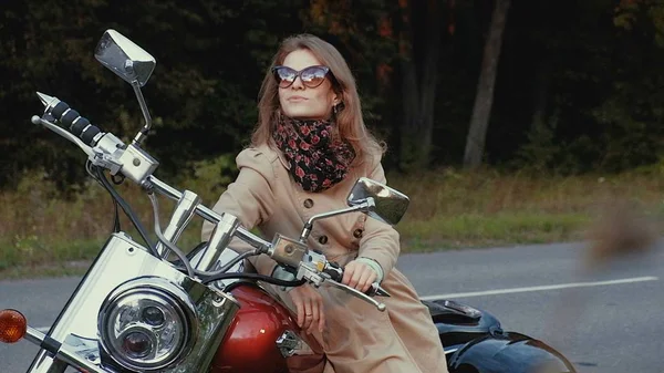 Jovem com cabelo castanho senta-se em uma moto perto de uma estrada . — Fotografia de Stock