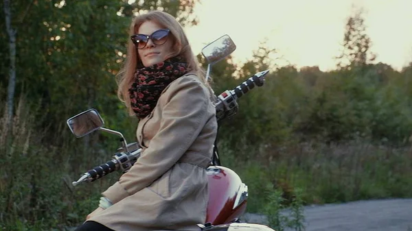 Jeune fille aux cheveux bruns s'assoit sur une moto près d'une route . — Photo