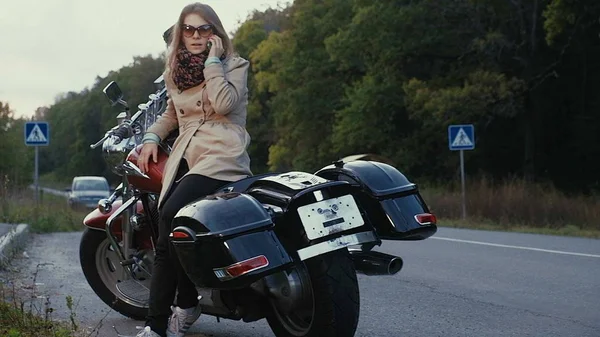 Chica joven con el pelo castaño se sienta en una moto cerca de una carretera . —  Fotos de Stock