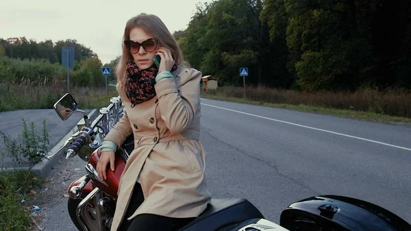 Mladá dívka s hnědými vlasy sedí na motorce v blízkosti silnice. — Stock fotografie