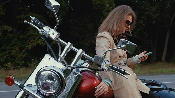 Chica joven con el pelo castaño se sienta en una moto cerca de una carretera . —  Fotos de Stock