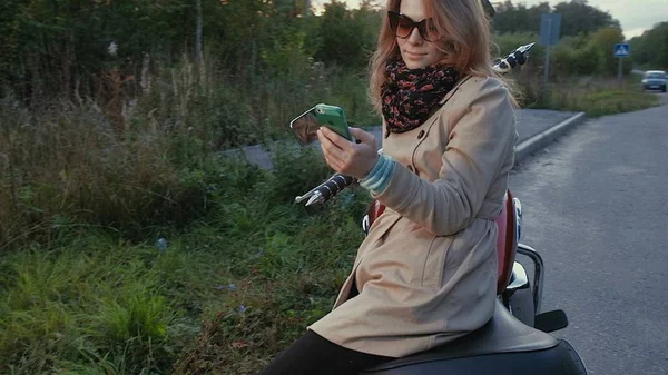 Chica joven con el pelo castaño se sienta en una moto cerca de una carretera . — Foto de Stock