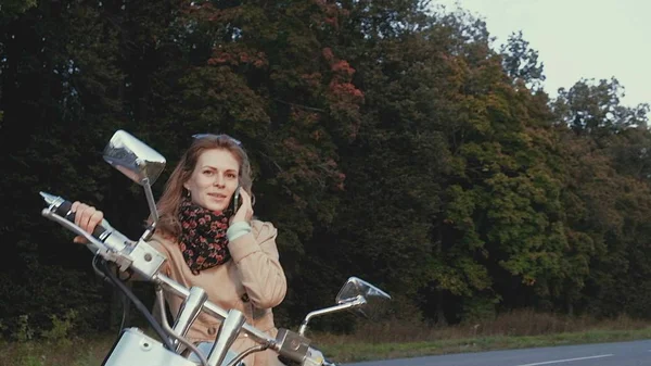 Jong meisje met bruine haren zit op een motor in de buurt van een weg. — Stockfoto