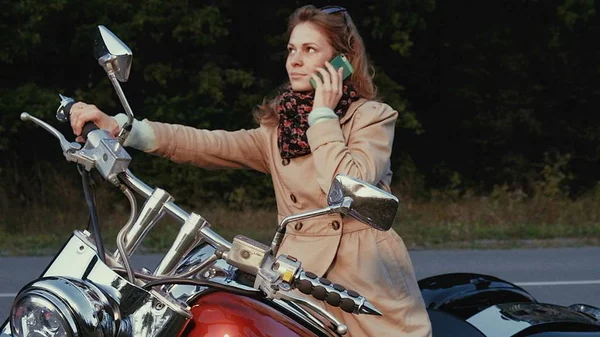 Jovem com cabelo castanho senta-se em uma moto perto de uma estrada . — Fotografia de Stock