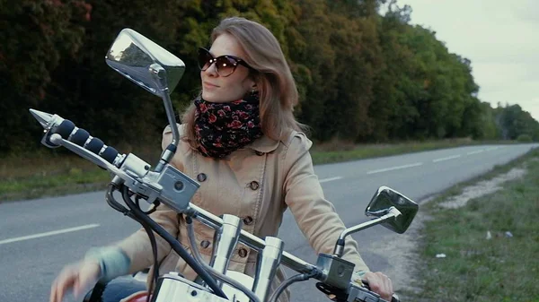 Jong meisje met bruine haren zit op een motor in de buurt van een weg. — Stockfoto