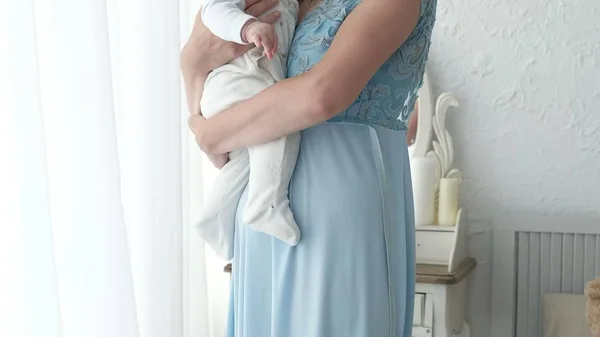 Seguindo a mãe colocando o bebê para dormir enquanto caminha. Mulher atraente segurando bebê em mãos e andar através da sala de estar com cortinas de janela brilhantes no fundo . — Fotografia de Stock