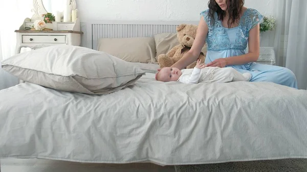 Seguindo a mãe colocando o bebê para dormir enquanto caminha. Mulher atraente segurando bebê em mãos e andar através da sala de estar com cortinas de janela brilhantes no fundo . — Fotografia de Stock