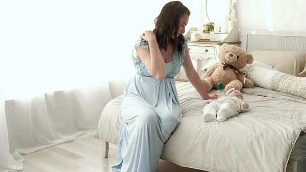 Seguindo a mãe colocando o bebê para dormir enquanto caminha. Mulher atraente segurando bebê em mãos e andar através da sala de estar com cortinas de janela brilhantes no fundo . — Fotografia de Stock