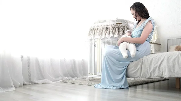 Seguindo a mãe colocando o bebê para dormir enquanto caminha. Mulher atraente segurando bebê em mãos e andar através da sala de estar com cortinas de janela brilhantes no fundo . — Fotografia de Stock