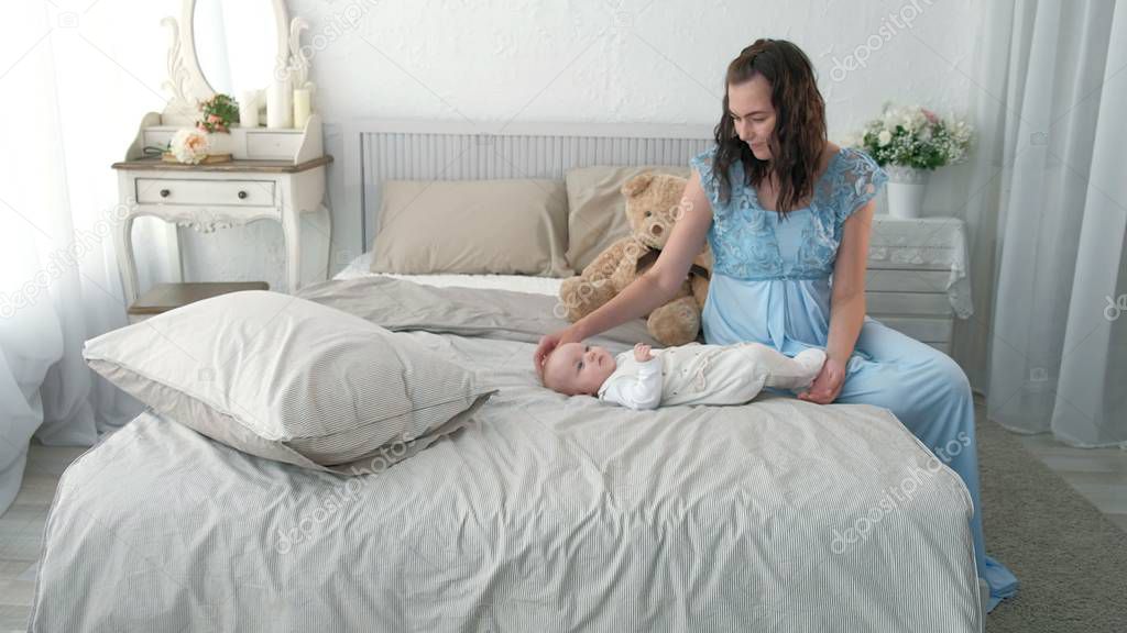 Tracking mother putting baby to sleep while walking . Attractive woman holding baby in hands and walk across living room with bright window curtains in background.