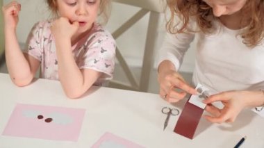 Bir kadın bir kızla renkli kağıttan bir masada evde oturan bir uygulama yapıyor