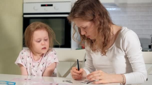 Eine Frau mit einem Mädchen bei einer Applikation von buntem Papier, die zu Hause an einem Tisch sitzt — Stockvideo