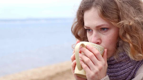 Romantiska unga kvinnan avslappnande på stranden med, dricka varmt te eller kaffe från termosen. Lugn och mysig kväll. — Stockfoto