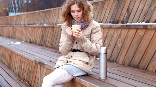 Romantica giovane donna che si rilassa sulla spiaggia con, bere tè caldo o caffè dal thermos. Serata tranquilla e accogliente . — Foto Stock