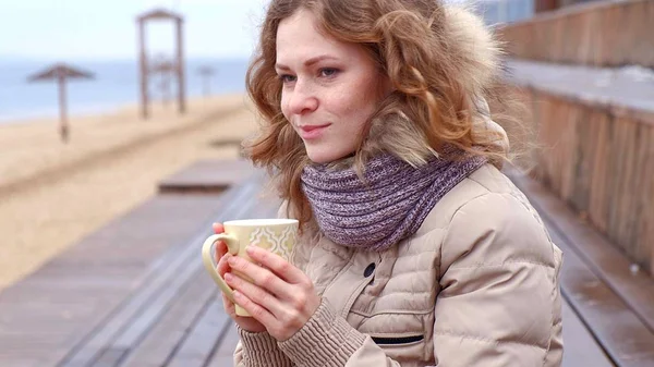Романтична молода жінка відпочиває на пляжі з, пити гарячий чай або каву з термоса. Спокійний і затишний вечір . — стокове фото