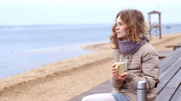 Романтичная молодая женщина отдыхает на пляже с, пить горячий чай или кофе из термоса. Спокойный и уютный вечер . — стоковое фото