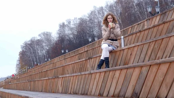 Romantický mladá žena relaxaci na pláži, pití horkého čaje nebo kávy z termosky. Klidný a příjemný večer. — Stock fotografie