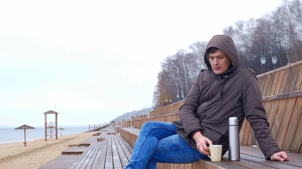 Романтичный молодой человек отдыхает на пляже с, пить горячий чай или кофе из термоса. Спокойный и уютный вечер . — стоковое фото