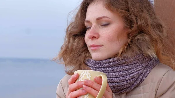 Romantische junge Frau, die es sich am Strand gemütlich macht, heißen Tee oder Kaffee aus der Thermoskanne trinkt. ruhiger und gemütlicher Abend. — Stockfoto