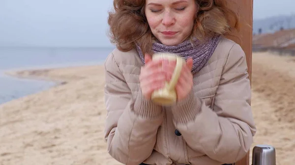 Romantikus fiatal nő pihentető a strandon, termosz iszik forró teát vagy kávét. Nyugodt és hangulatos esti. — Stock Fotó