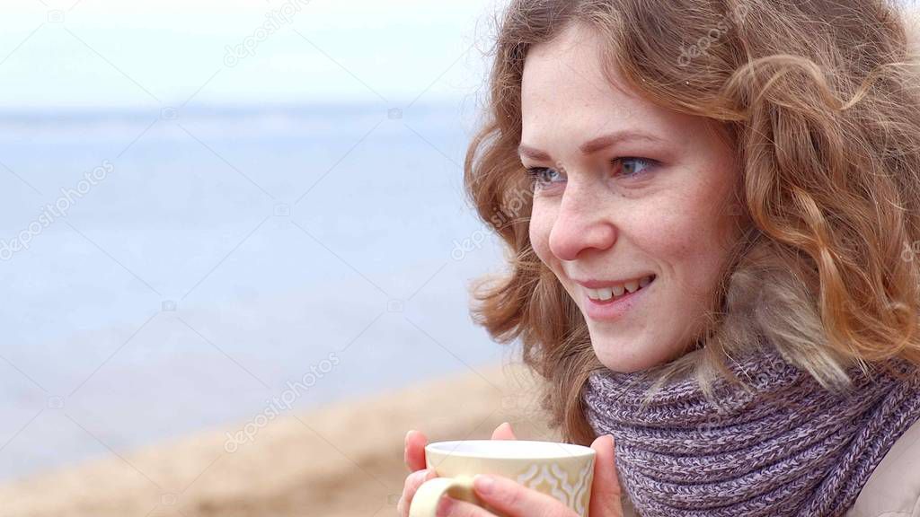 Romantic young woman relaxing on the beach with , drinking hot tea or coffee from thermos. Calm and cozy evening.