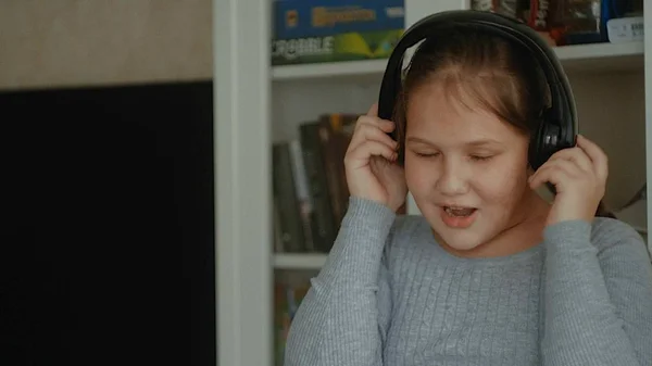Niña emocional. La niña con el pelo largo bailando con auriculares en una casa —  Fotos de Stock