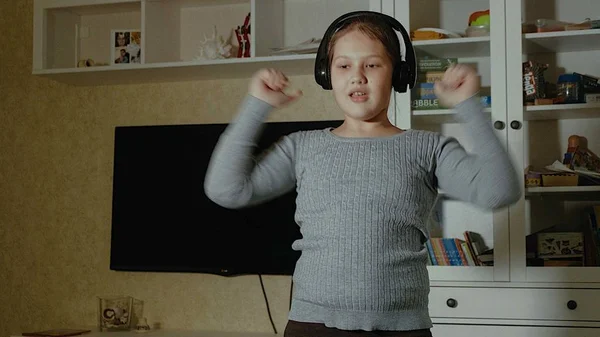 Niña emocional. La niña con el pelo largo bailando con auriculares en una casa —  Fotos de Stock