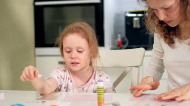 Bir kadın bir kızla renkli kağıttan bir masada evde oturan bir uygulama yapıyor