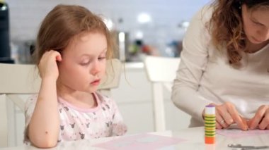 Bir kadın bir kızla renkli kağıttan bir masada evde oturan bir uygulama yapıyor