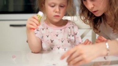 Bir kadın bir kızla renkli kağıttan bir masada evde oturan bir uygulama yapıyor