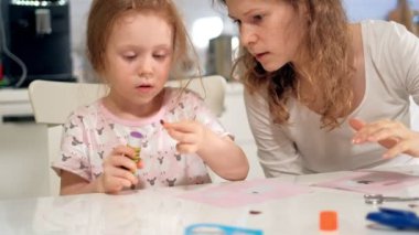 Bir kadın bir kızla renkli kağıttan bir masada evde oturan bir uygulama yapıyor