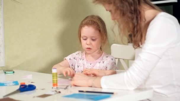 Μια γυναίκα με ένα κορίτσι που κάνει μια εφαρμογή από χρωματιστό χαρτί που κάθεται σε ένα τραπέζι στο σπίτι — Αρχείο Βίντεο