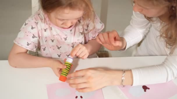 Eine Frau mit einem Mädchen bei einer Applikation von buntem Papier, die zu Hause an einem Tisch sitzt — Stockvideo