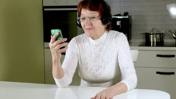 Starší žena poslouchá hudbu ve sluchátkách od telefonu, gestikuloval energicky a tančí — Stock video
