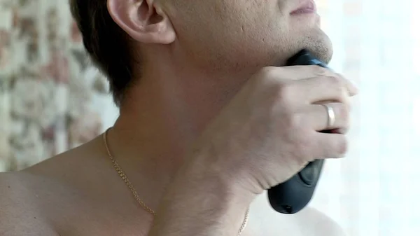 Uomo barba da barba con rasoio elettrico. Controlla la rasatura strisciando il dito sulla guancia. Primo piano . — Foto Stock