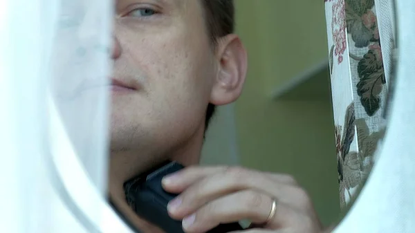 Muž holení vousů s elektrický holicí strojek. Podívejte, holení, tažením prstu na tvář. Closeup. — Stock fotografie