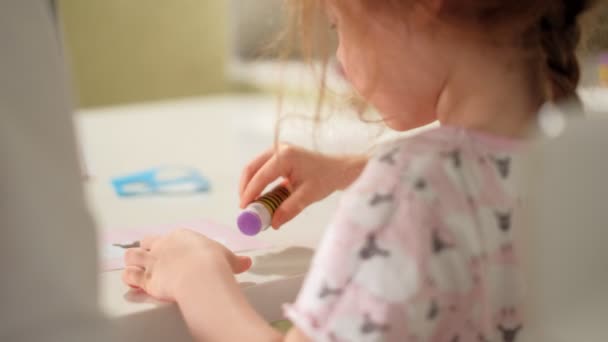 Μια γυναίκα με ένα κορίτσι που κάνει μια εφαρμογή από χρωματιστό χαρτί που κάθεται σε ένα τραπέζι στο σπίτι — Αρχείο Βίντεο