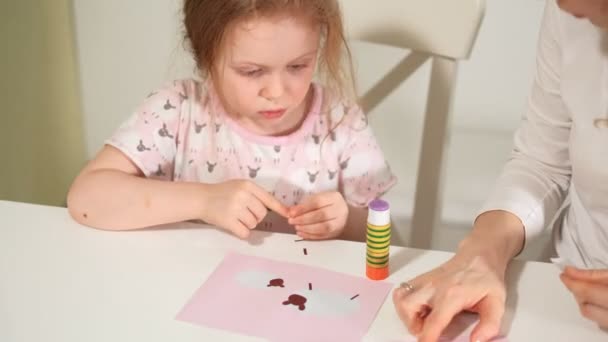 Una mujer con una chica haciendo una aplicación de papel de color sentada en una mesa en casa — Vídeos de Stock