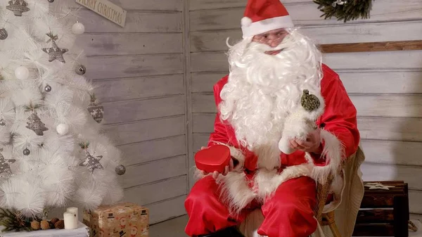 Weihnachtsmann sitzt in einem Stuhl und versucht, ein Spielzeug als Geschenk zu stopfen — Stockfoto