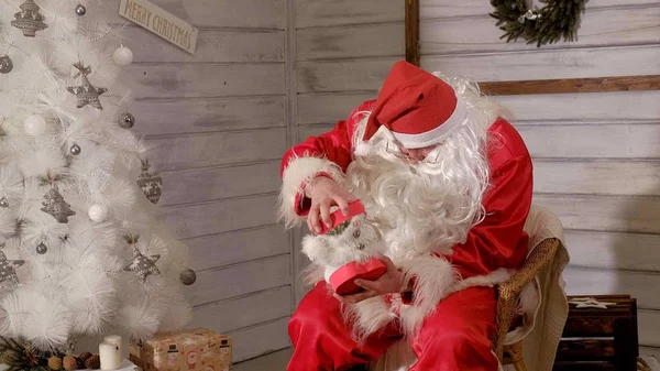Santa jest siedzi na krześle i stara się rzeczy zabawka na prezent — Zdjęcie stockowe