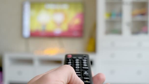 Mão segurar TV controle remoto. TV no fundo . — Vídeo de Stock