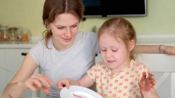 Familia feliz, madre e hija pequeña pintan con pintura en platos blancos — Vídeos de Stock