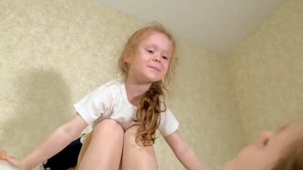 Beautiful mother and daughter embrace and play at home in the bedroom on the bed — Stock Video